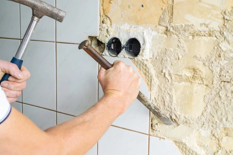 Hands removing kitchen tile using a hammer and chisel