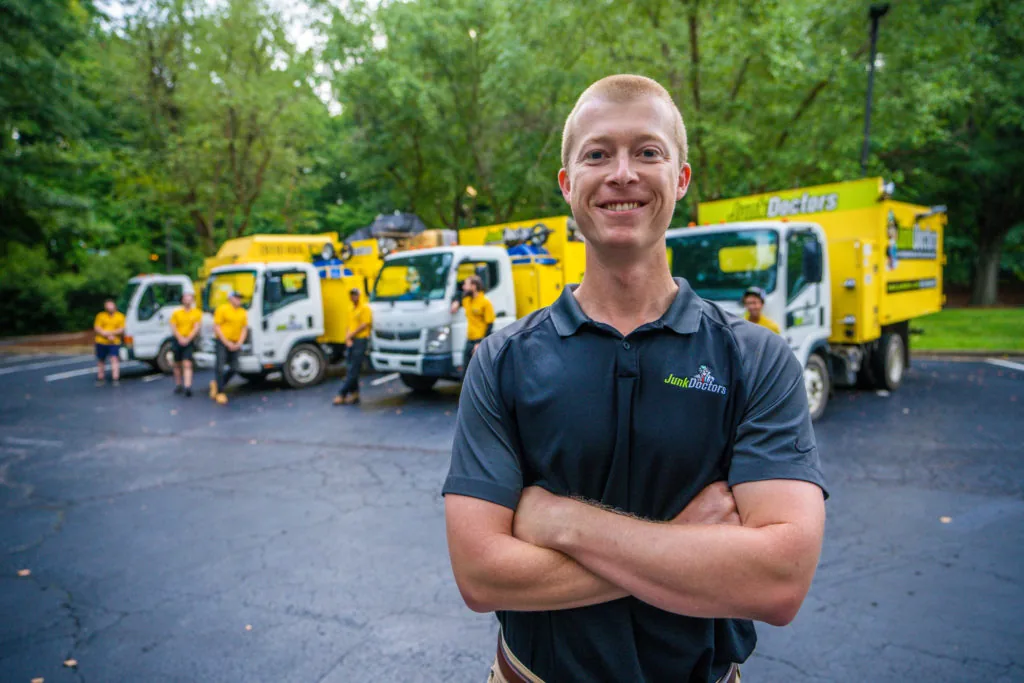 Smiling junk removal professional in front of a row of junk removal trucks